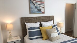 A neatly made bed with striped bedding, a wicker headboard, and two bedside tables with lamps. - The Hideaway- Cozy Home in the Woods (Hot Springs)