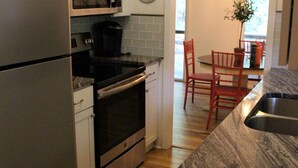 A kitchen with a stainless steel refrigerator, a built-in oven, a microwave, and a sink. There is a clock on the wall and a plant in the dining area. - The Hideaway- Cozy Home in the Woods (Hot Springs)
