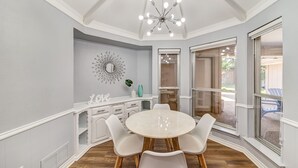 A dining area with a round table, white chairs, a chandelier, a decorative mirror, and a window with a view of the outdoors. - Near Highways, King bed, Family-friendly, Remote work, Foosball, Grill, Games (Carrollton)