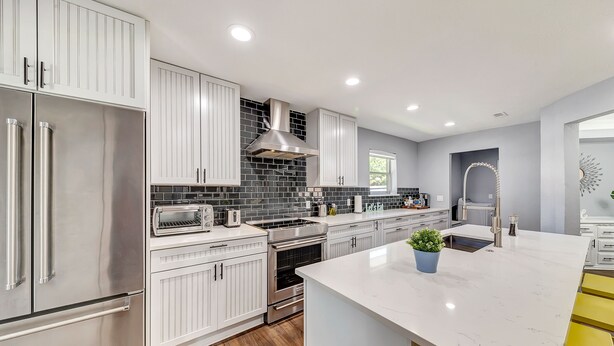 A modern kitchen with white cabinetry, stainless steel appliances, a black tiled backsplash, and a marble countertop. - Near Highways, King bed, Family-friendly, Remote work, Foosball, Grill, Games (Carrollton)