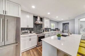A modern kitchen with white cabinetry, stainless steel appliances, a black tiled backsplash, and a marble countertop. - Near Highways, King bed, Family-friendly, Remote work, Foosball, Grill, Games (Carrollton)