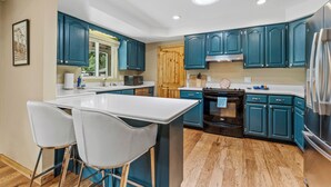 Una cucina moderna con armadietti color petrolio, un'isola centrale con sgabelli da bar, un forno integrato e un frigorifero in acciaio inossidabile.