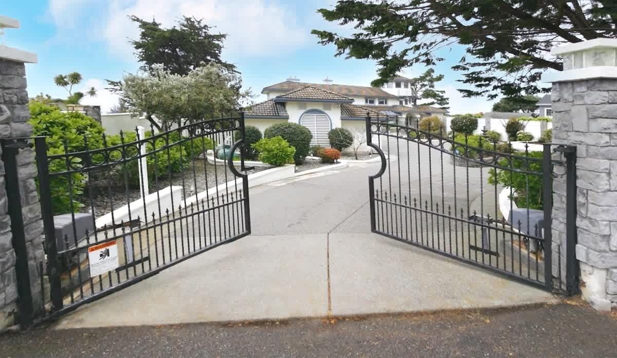 A gated driveway leading to a residential property with a stone wall on one side and a metal gate.