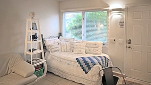 A bedroom with a bed, a white chair, a small table, a white shelf with books, and a window with blinds. - Sparkling Clean, Private & Quiet! Amazing Ocean Views [6] (Brookings)