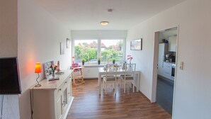 Cozinha moderna com área de jantar, piso de madeira e vista através de grandes janelas.
