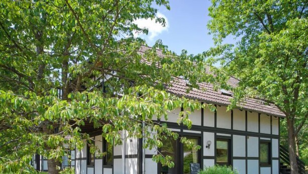 Un bâtiment traditionnel avec un toit en tuiles, entouré d’arbres et de verdure.