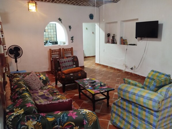 A living room with a sofa, armchairs, a coffee table, and a TV mounted on the wall.