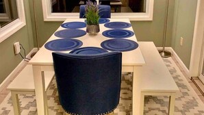 Un coin repas avec une table rectangulaire dressée pour quatre personnes, flanquée de deux chaises, d’une plante en pot et d’une grande fenêtre.