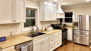 Une cuisine moderne avec des meubles blancs, des appareils en acier inoxydable et un plan de travail en bois.