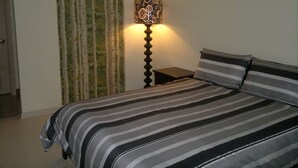 A bedroom with a bed, striped bedding, a lamp, and a curtain. - SM FIELD RESIDENCES, 85m2, FREE POOL, 2 BEDROOMS, 2 BATHROOMS, 24HRS SECURITY (Sucat)
