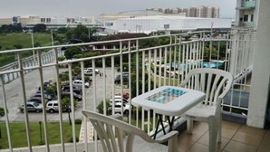A balcony with a table and chairs, overlooking a parking lot and buildings. - SM FIELD RESIDENCES, 85m2, FREE POOL, 2 BEDROOMS, 2 BATHROOMS, 24HRS SECURITY (Sucat)