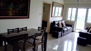 A spacious living room with a dining area, a black leather sofa, a ceiling fan, and large windows. - SM FIELD RESIDENCES, 85m2, FREE POOL, 2 BEDROOMS, 2 BATHROOMS, 24HRS SECURITY (Sucat)