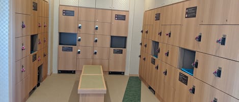 A locker room with multiple wooden lockers, a central bench, and a green carpet strip.