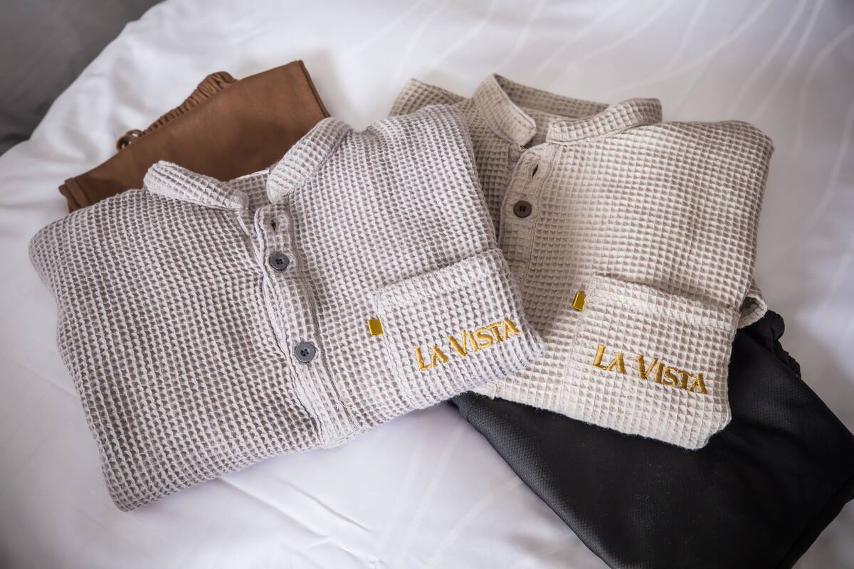 Dos camisas dobladas con orden, con el bordado "LA VISTA", sobre una cama blanca.