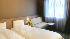 Habitación de hotel con dos camas grandes, un pequeño sofá, una mesa redonda y una ventana con cortinas.