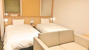 A hotel room with two beds, a nightstand with a clock, and a seating area.