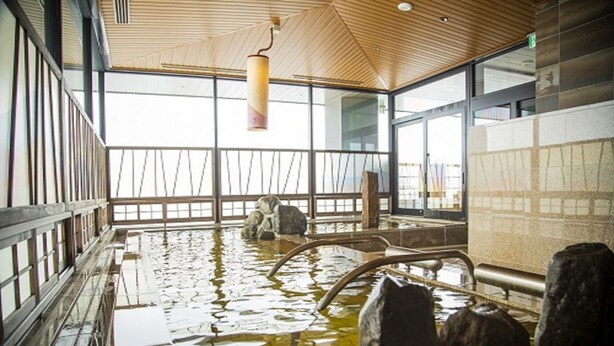 Una piscina interior con paredes de vidrio transparente, techo de madera y grandes rocas.