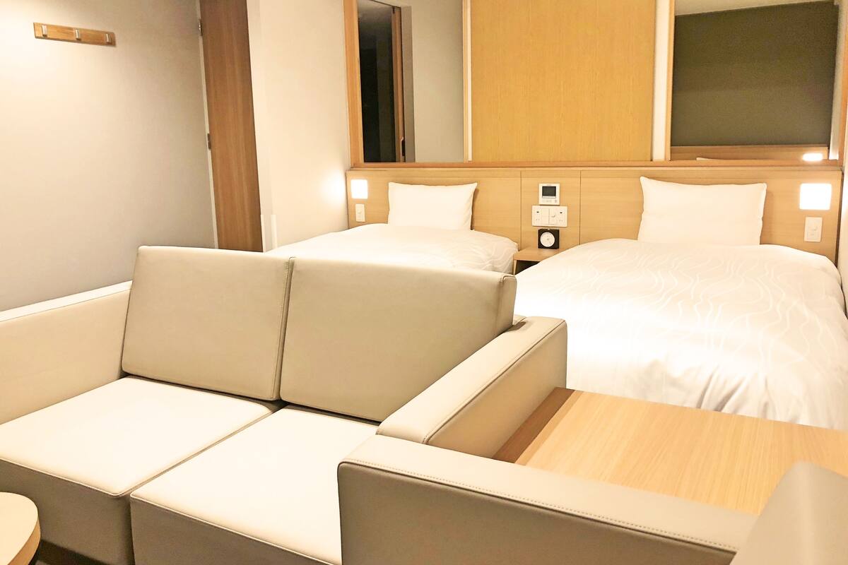 Una habitación de hotel con sofá, cama, mesita de noche y espejo.