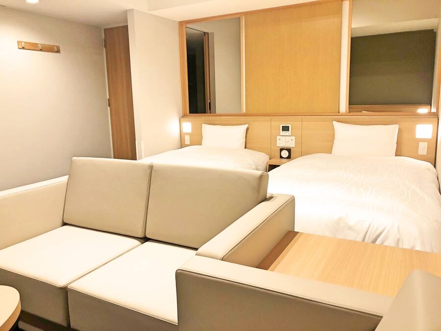 Quarto de hotel com sofá, cama, mesa de cabeceira e espelho.