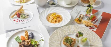 Una mesa servida con diversos platos, como pasta, mariscos y verduras, junto con tazas de café y una carta.