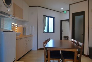 A compact kitchen with a dining area, featuring a wooden table and chairs, a window, and a microwave above the counter. - West Villa (Naha)
