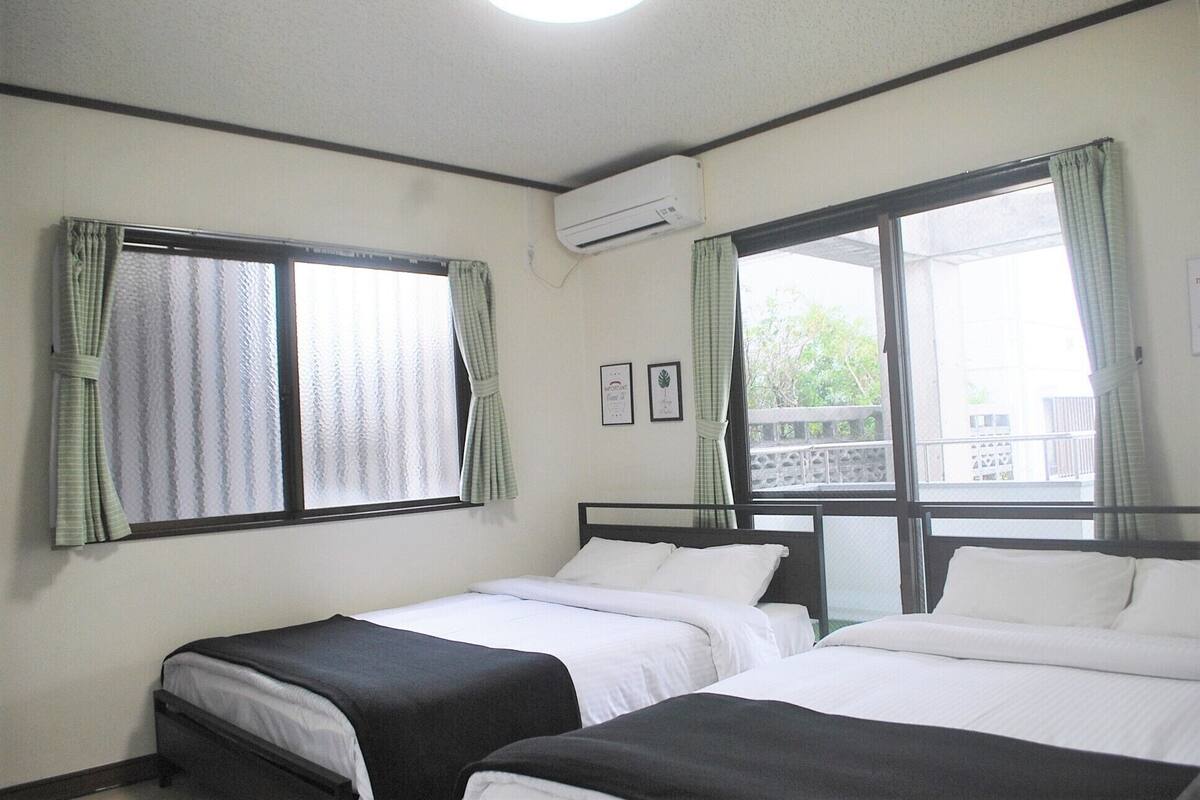 Habitación de hotel con dos camas individuales, ventana con cortinas, aire acondicionado y un pequeño balcón.