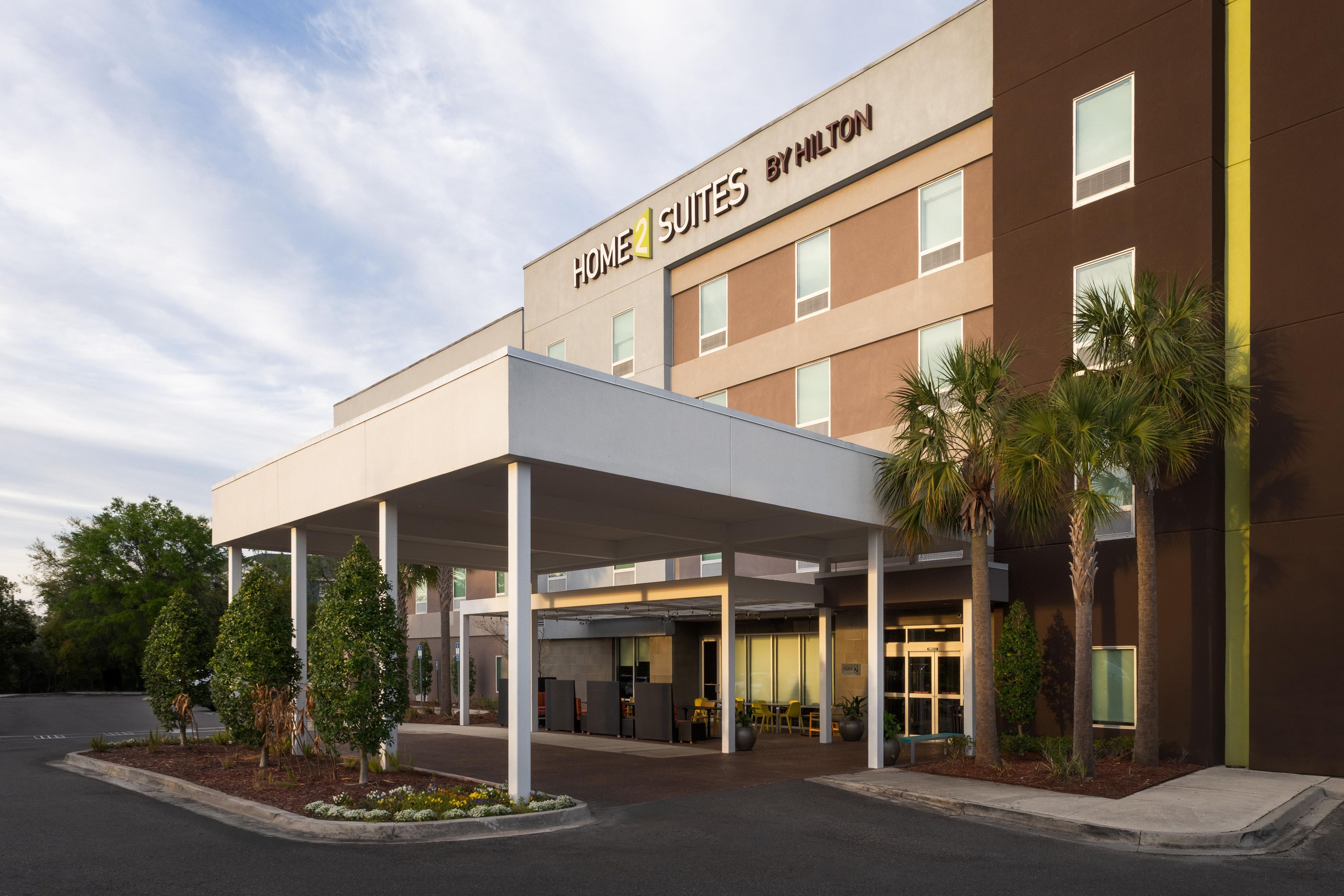 A hotel with a covered entrance, outdoor seating, and palm trees.