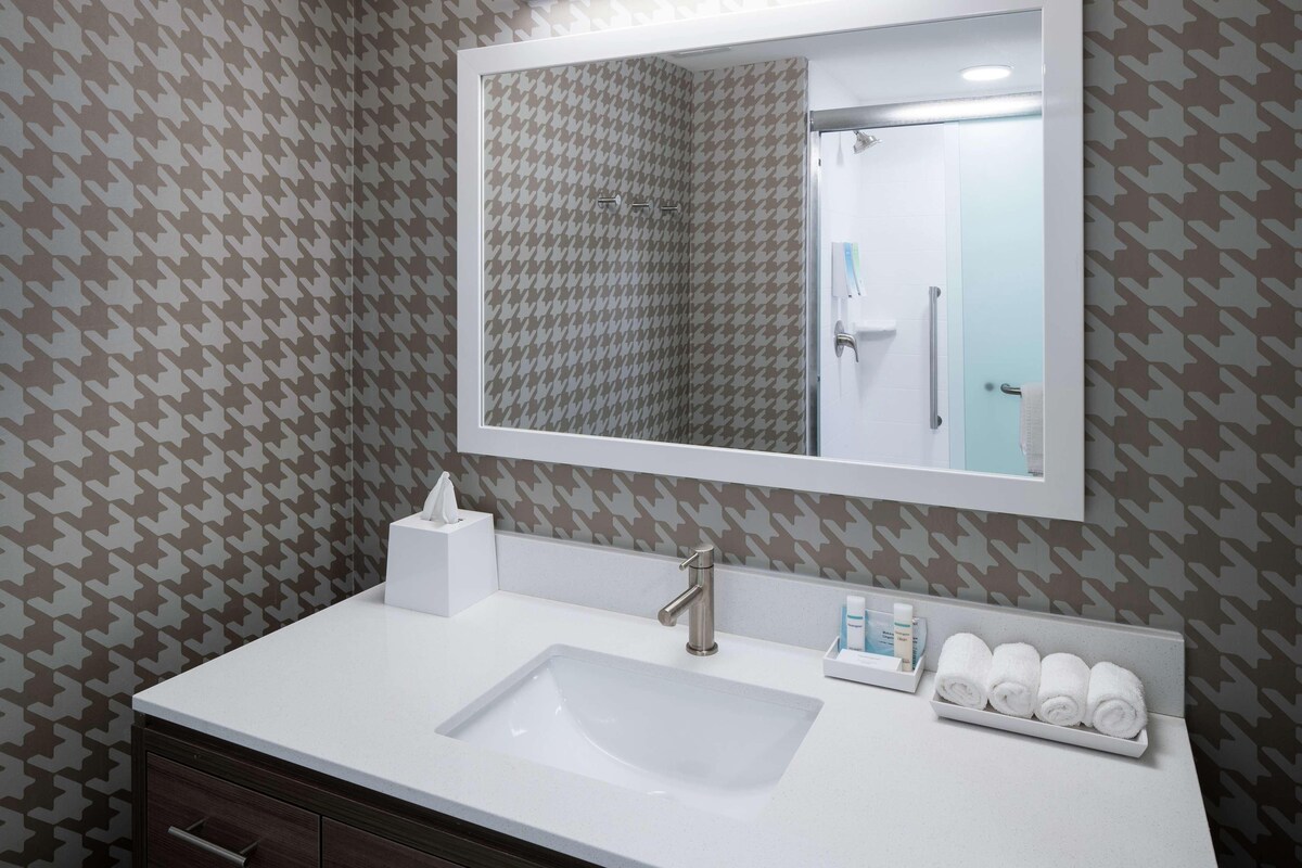 A bathroom with a white sink, a mirror, and patterned wallpaper.