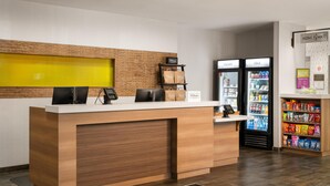 A hotel reception desk with a wooden counter, a digital display, a cash register, and a minibar. - Home2 Suites by Hilton Jacksonville Airport (Jacksonville)