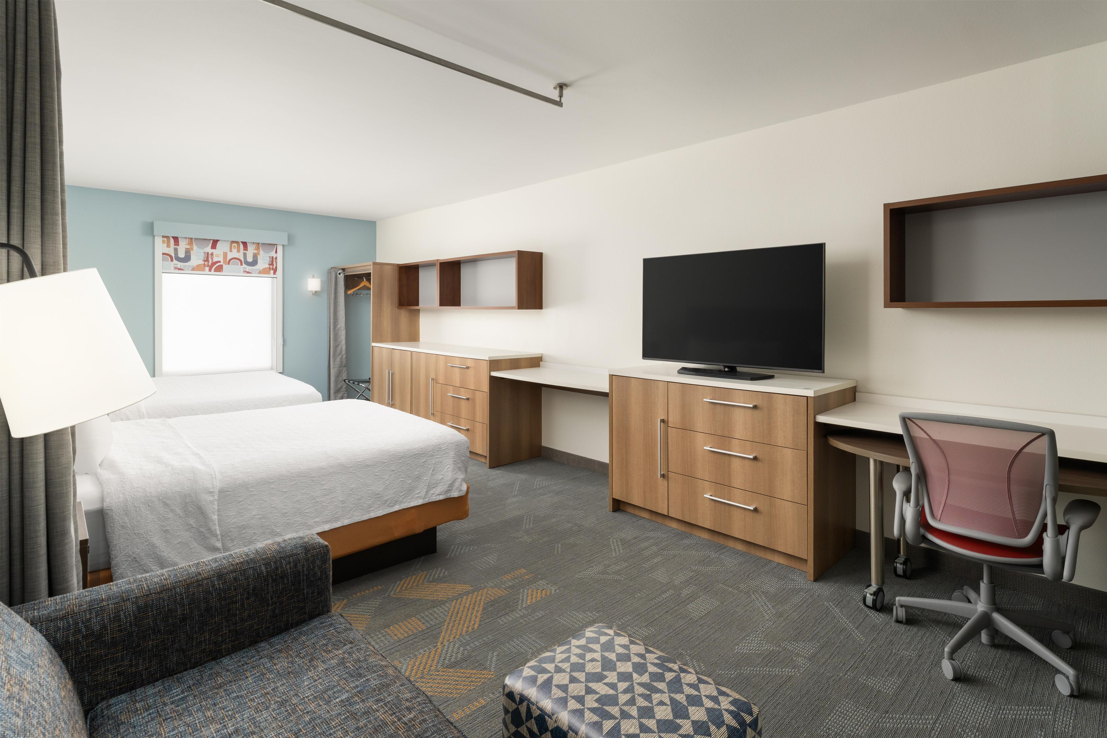 A hotel room with a bed, a desk, a television, a chair, and a small table.