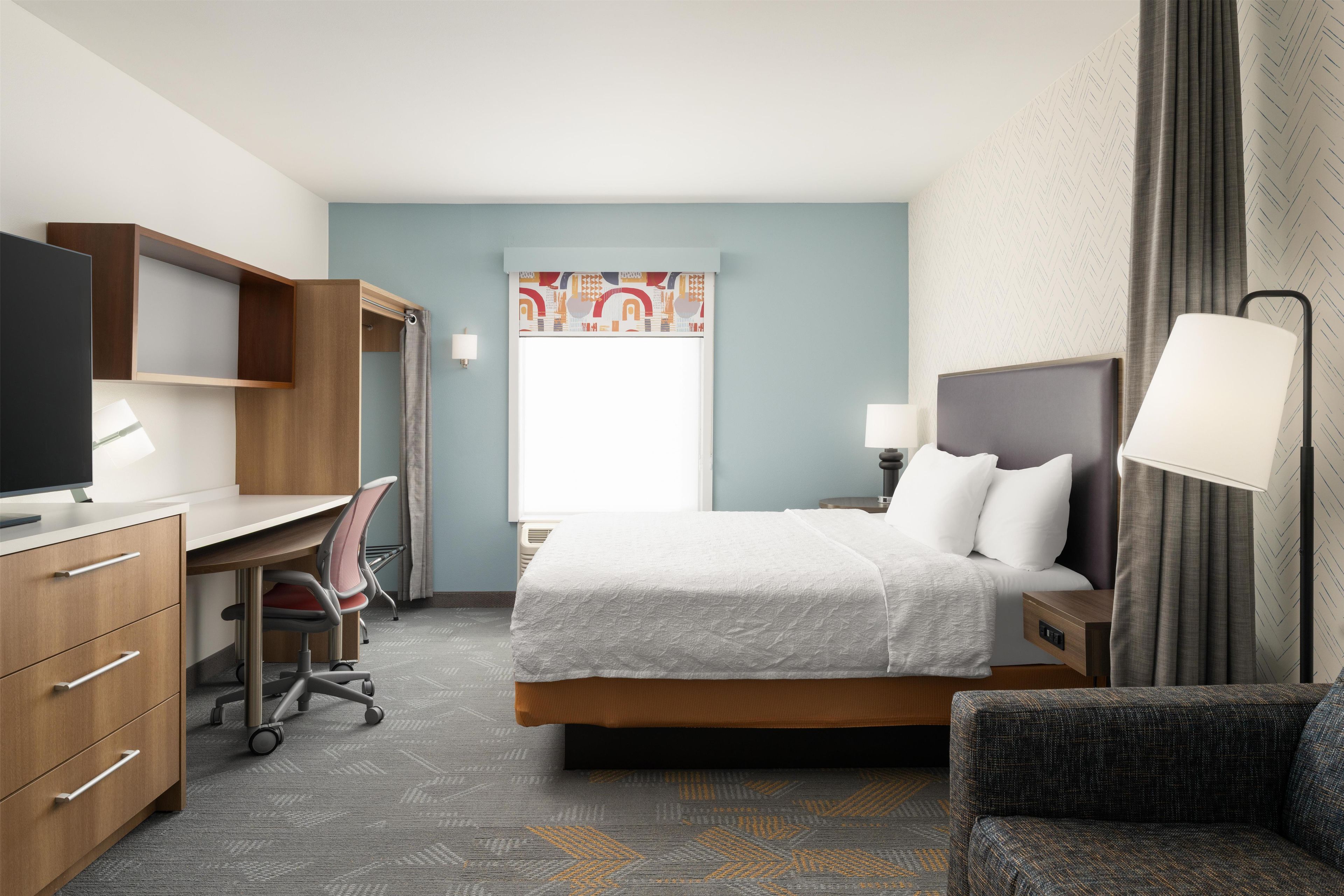 A hotel room with a bed, desk, chair, and a television.