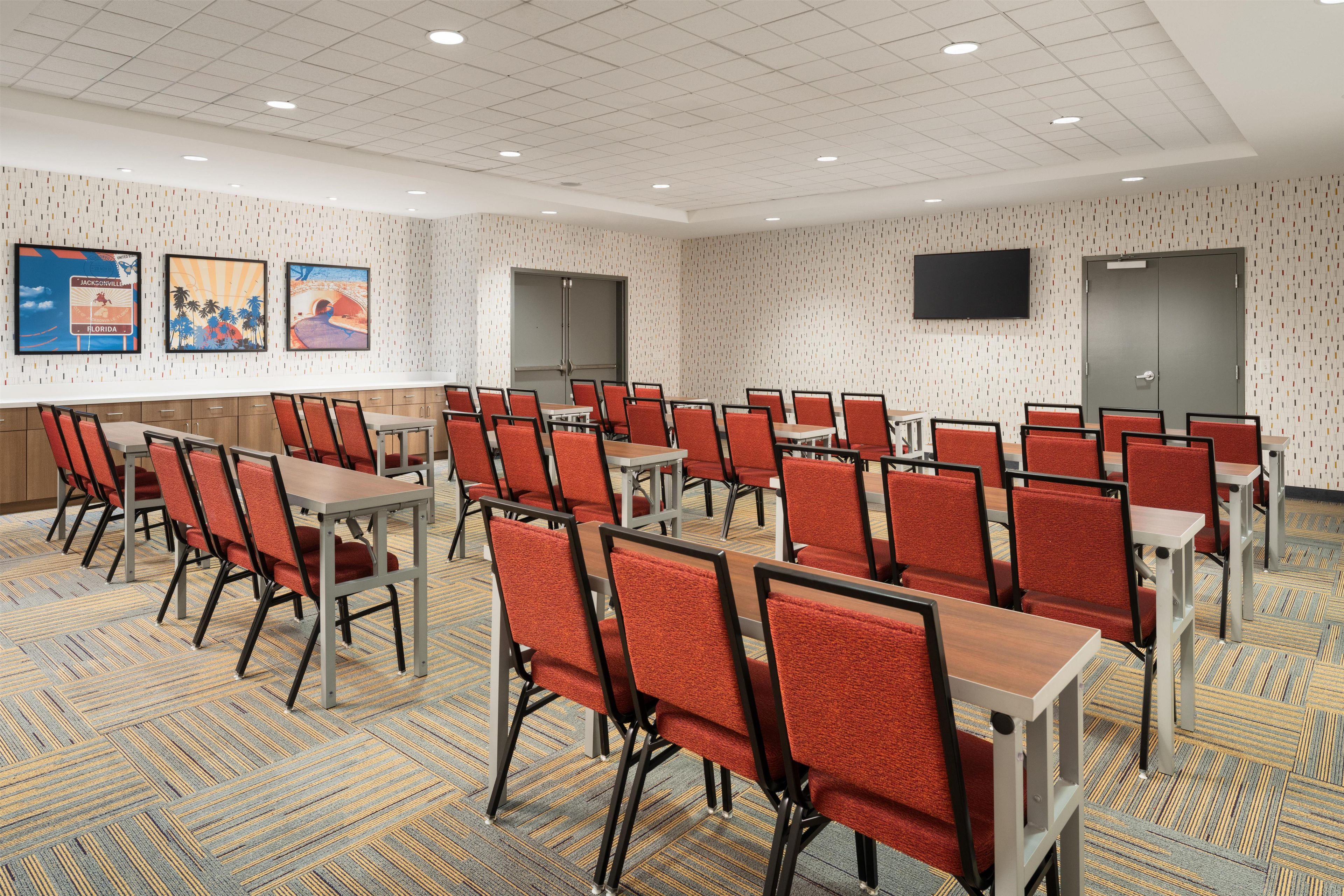 A conference room with multiple tables and chairs, a flat-screen TV mounted on the wall, and patterned wallpaper.