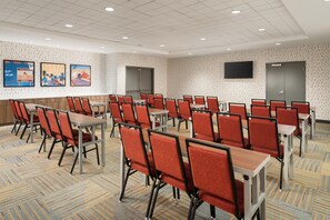 Une salle de conférence dotée de plusieurs tables et chaises, d’un téléviseur à écran plat fixé au mur et d’un papier peint à motifs.