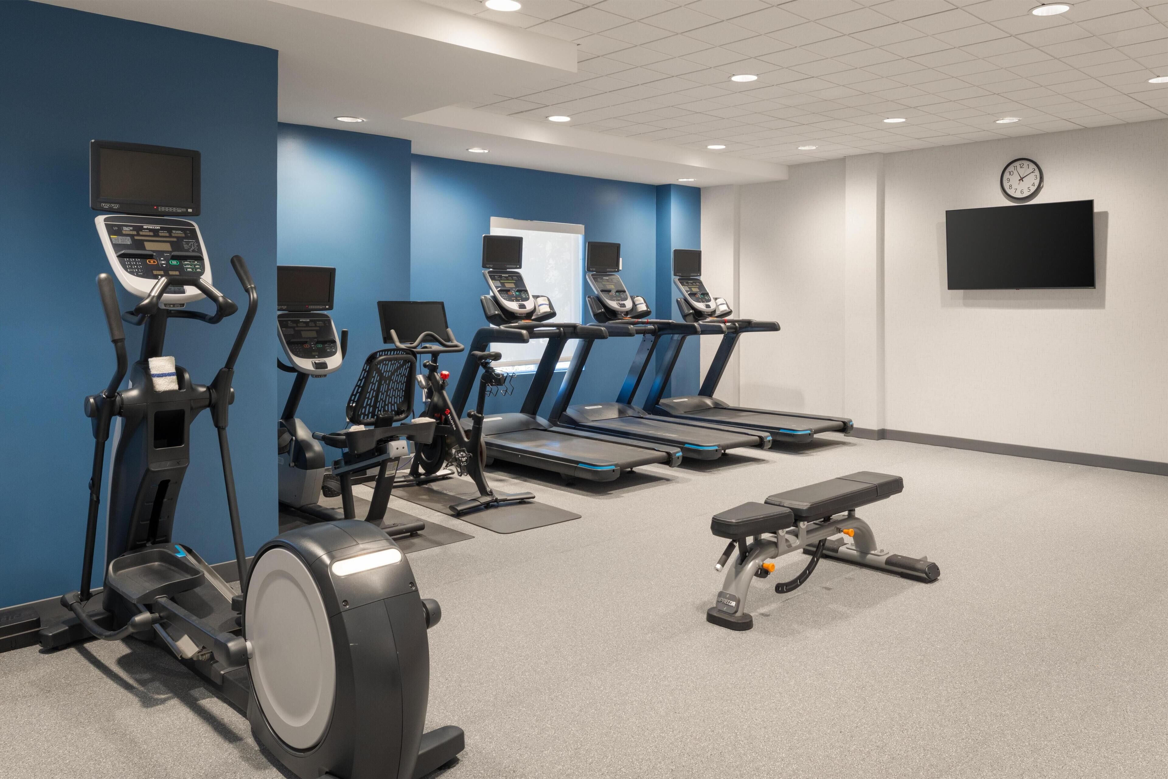 A gym with treadmills, elliptical machines, and a bench.