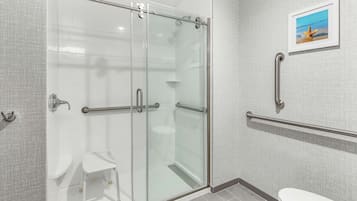 Un baño moderno con cabina de ducha de vidrio, inodoro blanco y un taburete blanco pequeño.