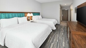 A hotel room with two beds, a wooden headboard, a flat-screen TV, and a carpeted floor.