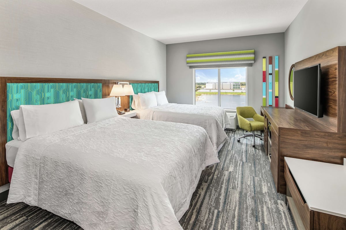 A hotel room with two beds, a desk, a chair, a TV, and a window with a view.