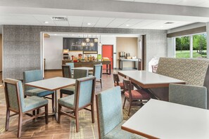 A modern dining area with tables and chairs, a kitchen counter, and a view of the outdoors. - Hampton Inn Odessa Trinity (Trinity)