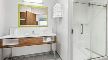 A modern bathroom with a white sink, wooden vanity, a mirror with a green frame, and a glass shower enclosure.