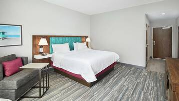 A hotel room with a bed, a sofa, a small table, a nightstand, and a wall-mounted sink.