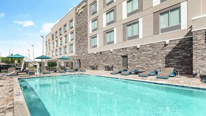 A hotel with a swimming pool, lounge chairs, and umbrellas.