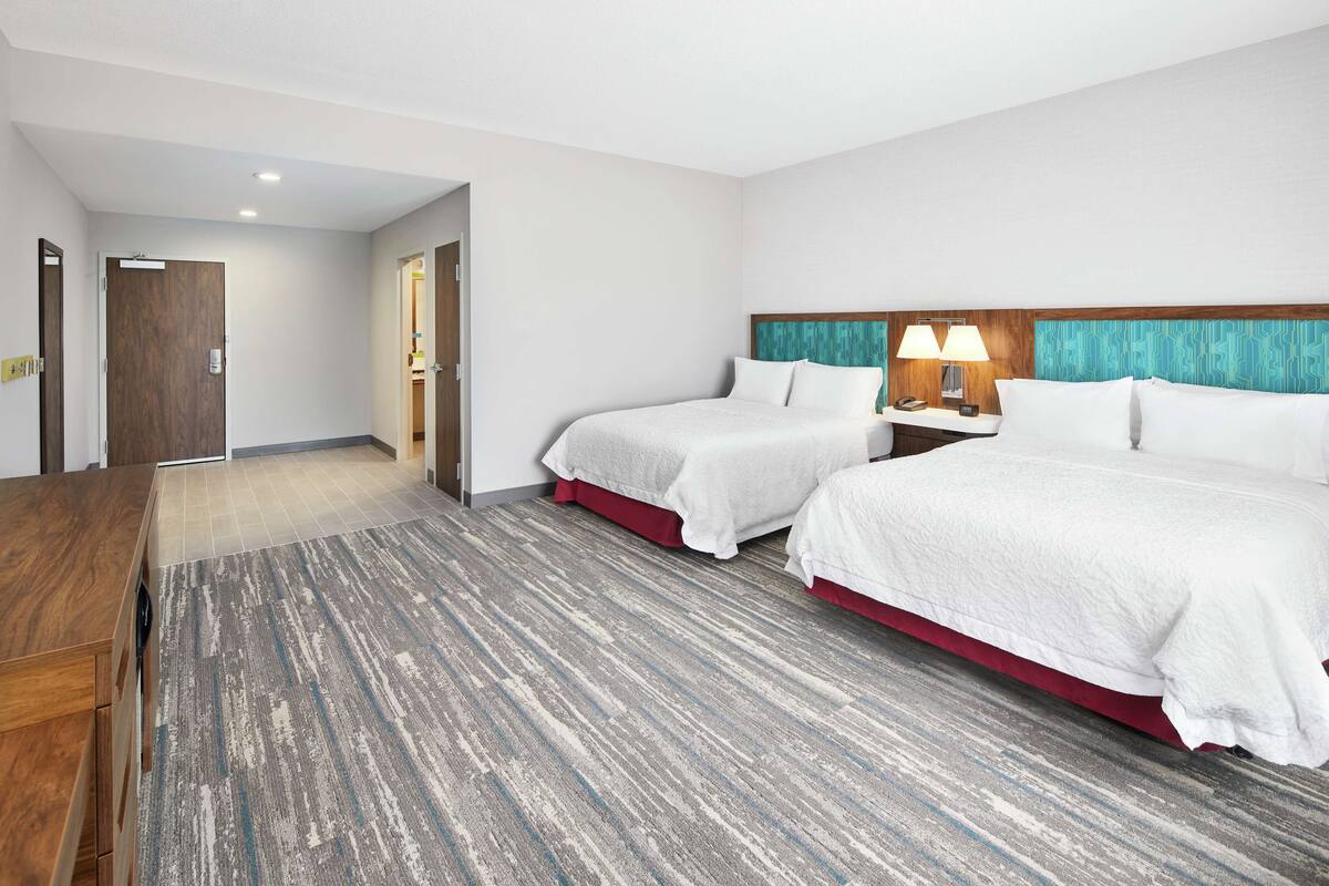 A hotel room with two beds, a wooden desk, and a carpeted floor.