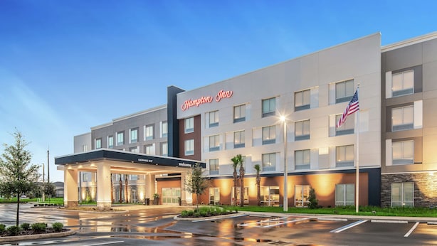 A Hampton Inn hotel with a modern exterior, a covered entrance, and an American flag.
