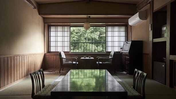 A traditional Japanese-style room with tatami flooring, a low table, and a view of greenery through large windows.