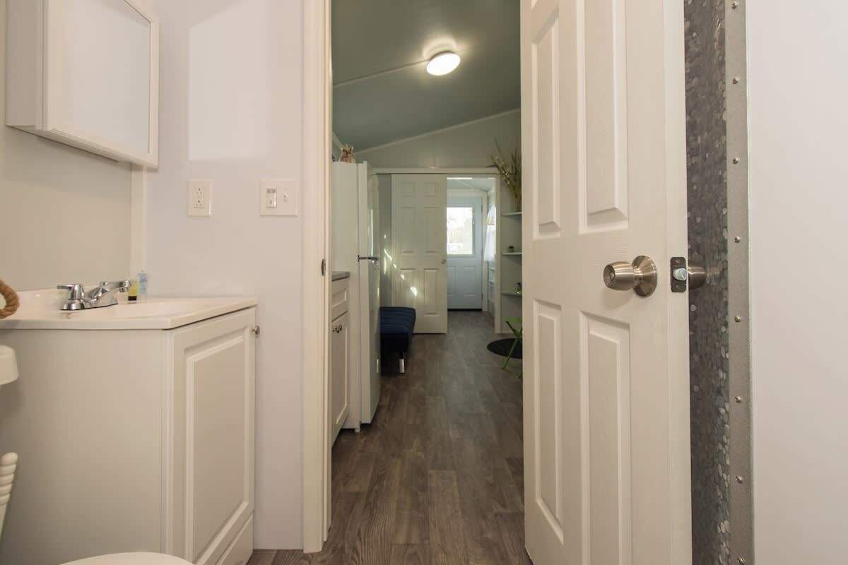 A hallway leading to a bedroom with a door on the right, a bathroom with a sink and toilet on the left, and a small bench in the middle.