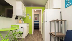 Une cuisine compacte avec un mur vert, des meubles blancs, une petite table à manger avec une chaise verte et un canapé bleu.