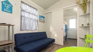 Ein Zimmer mit einem blauen Sofa, einem grünen Sessel, einer weißen Tür und einem Fenster mit Moskitonetz.