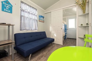 Een kamer met een blauwe bank, een groene stoel, een witte deur en een raam met een vliegenhor.