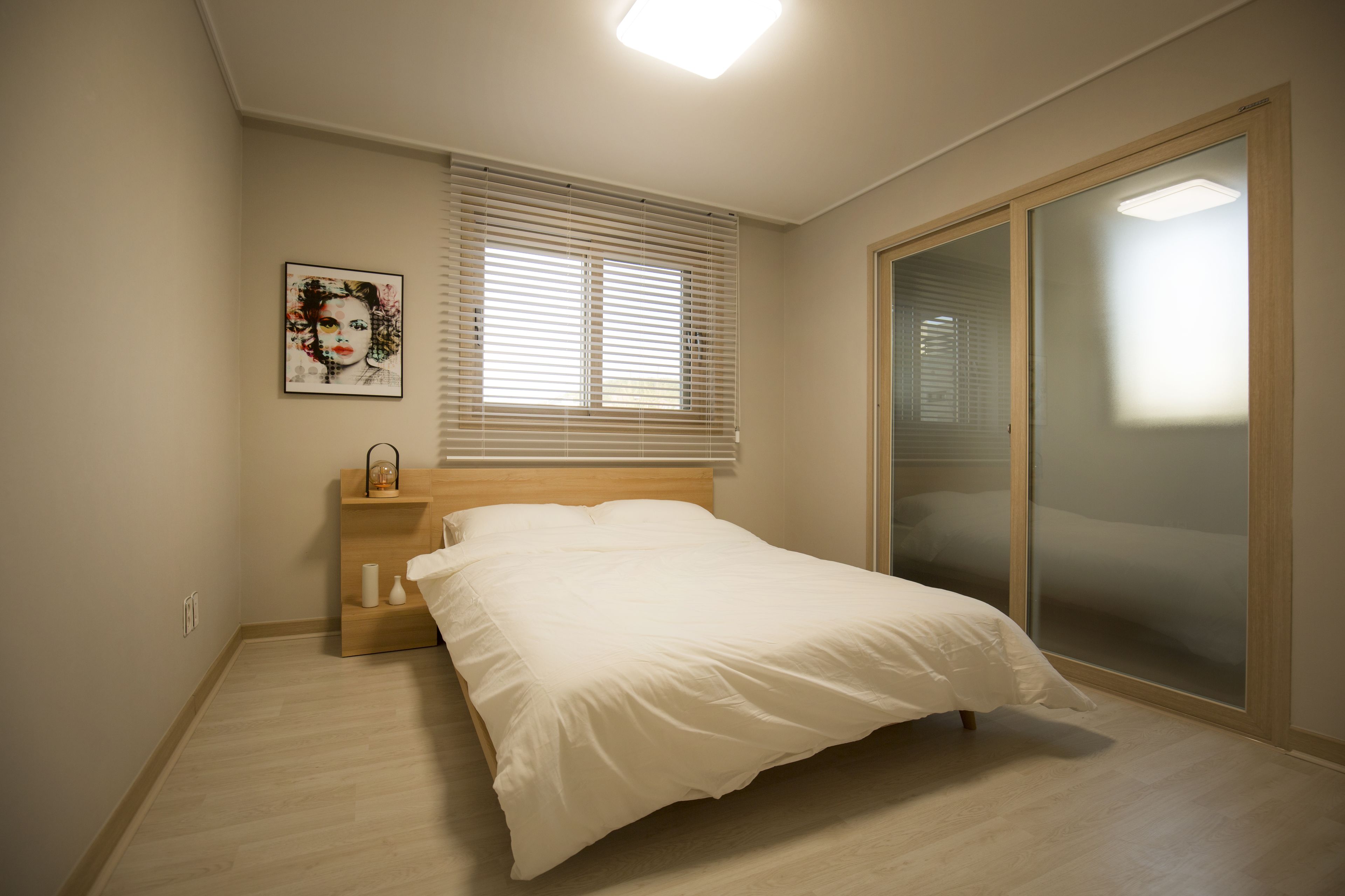 A bedroom with a bed, a nightstand, a window with blinds, and a sliding glass door.