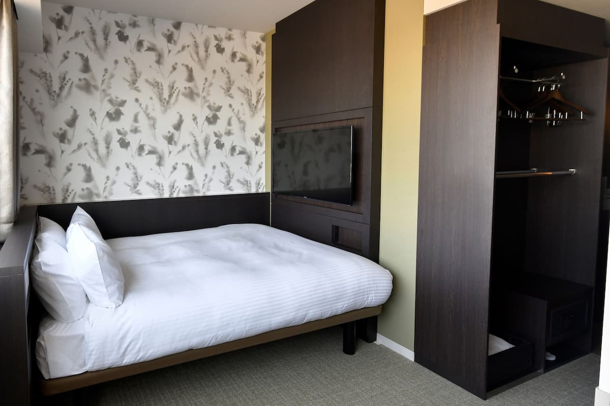 A hotel room with a bed, a TV, a wardrobe, and a window.